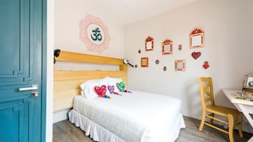 Un dormitorio con cabecera de madera, ropa de cama blanca, un escritorio con silla y decoración en la pared que incluye una mandala y fotografías enmarcadas.
