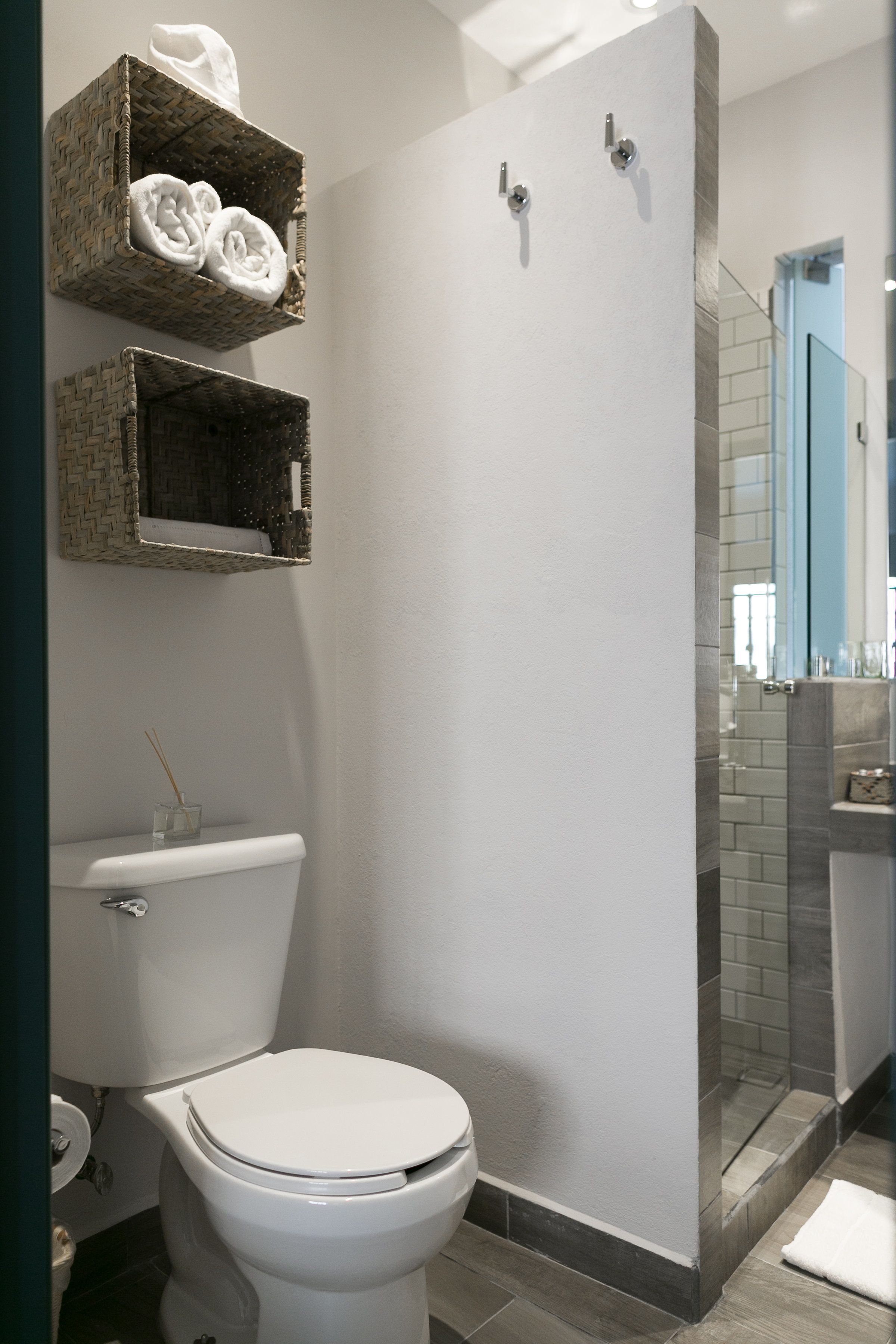 A bathroom with a white toilet, a shower enclosure, and two wicker baskets on the wall.