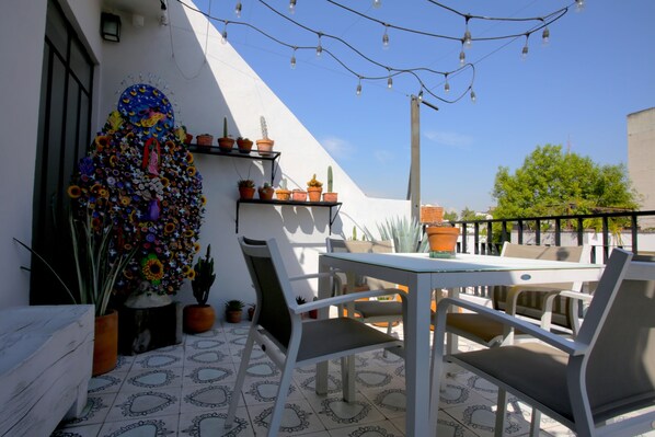 Eine Terrassengruppe im Freien mit weißem Tisch und Stühlen, umgeben von Blumentöpfen und einer dekorativen Wand.