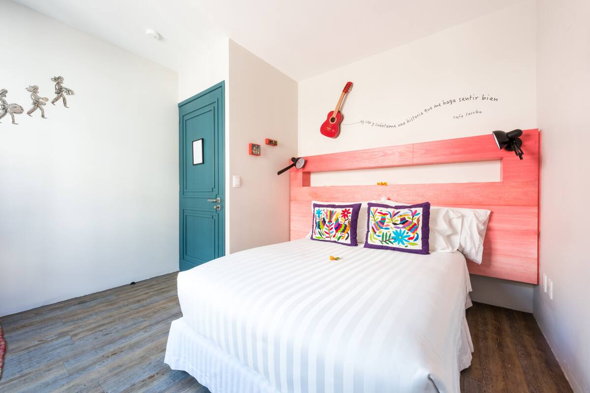 Un dormitorio con una cama, una puerta color turquesa y una guitarra en la pared.