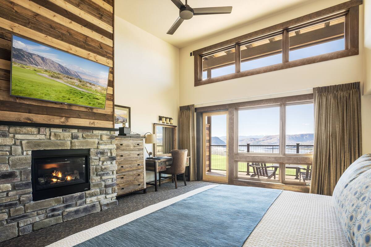 A spacious room with a stone fireplace, a desk with a chair, and a large window overlooking a scenic view.
