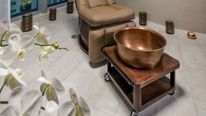 Una habitación moderna con un ventanal grande, un sillón reclinable, un cuenco de cobre sobre un carrito y orquídeas blancas.