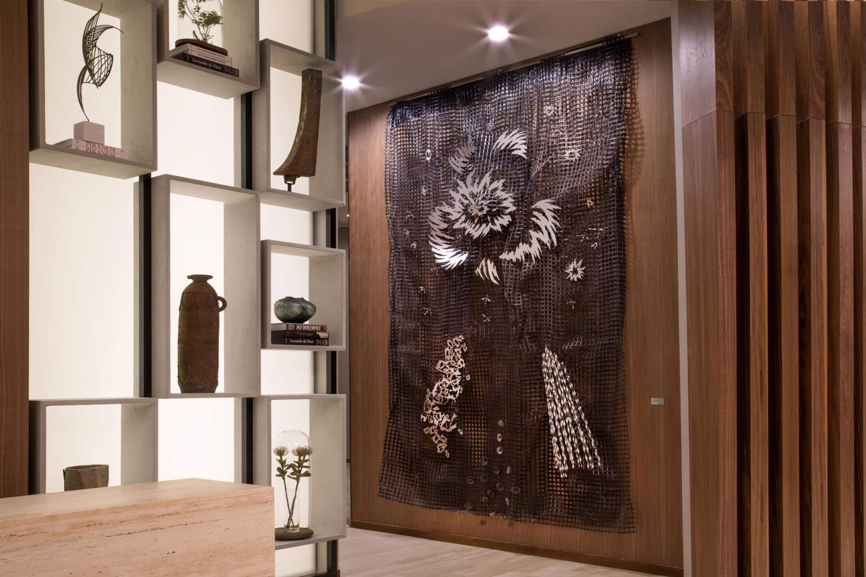 Un interior moderno con un panel de madera, una escultura metálica decorativa y una estantería minimalista con diversos objetos.