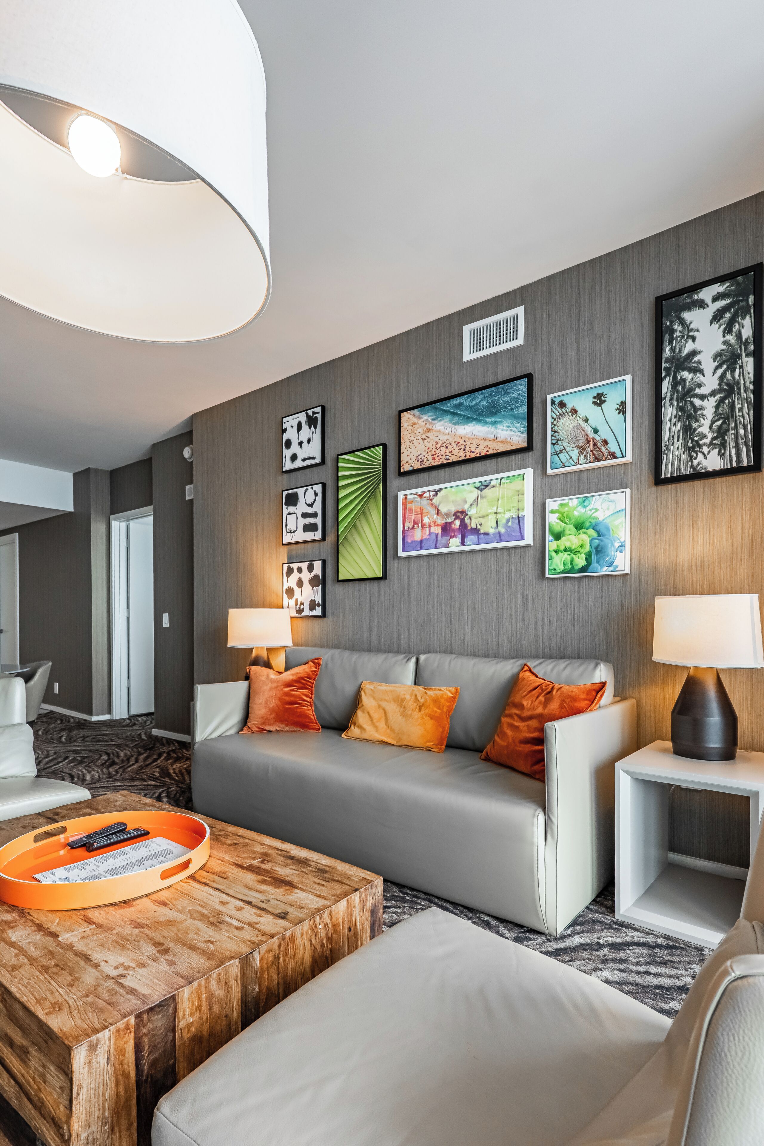 Una sala de estar moderna con un sofá gris, cojines naranja, una mesa de centro de madera y un televisor montado en la pared.