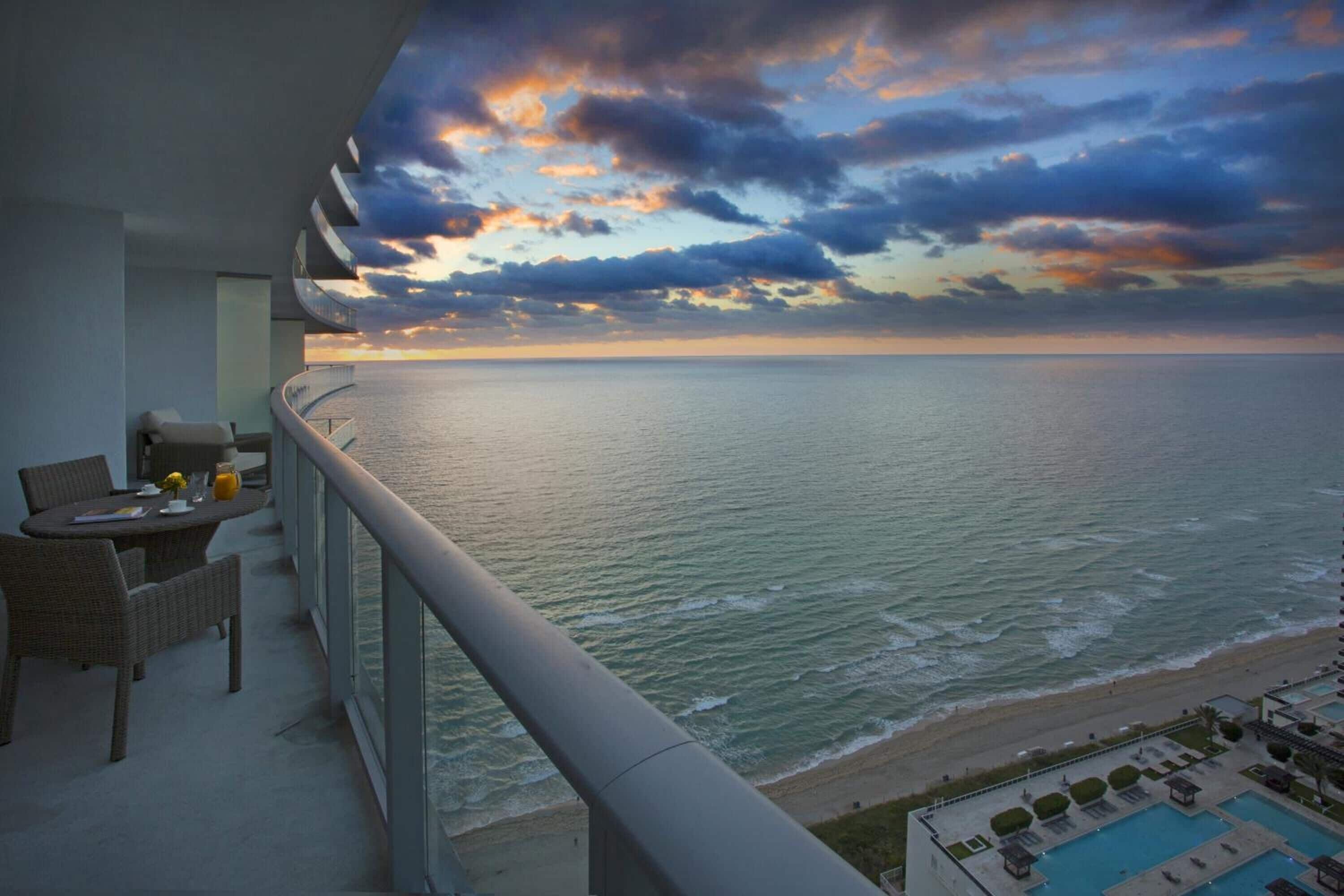 A balcony with a view of the ocean and a pool area.