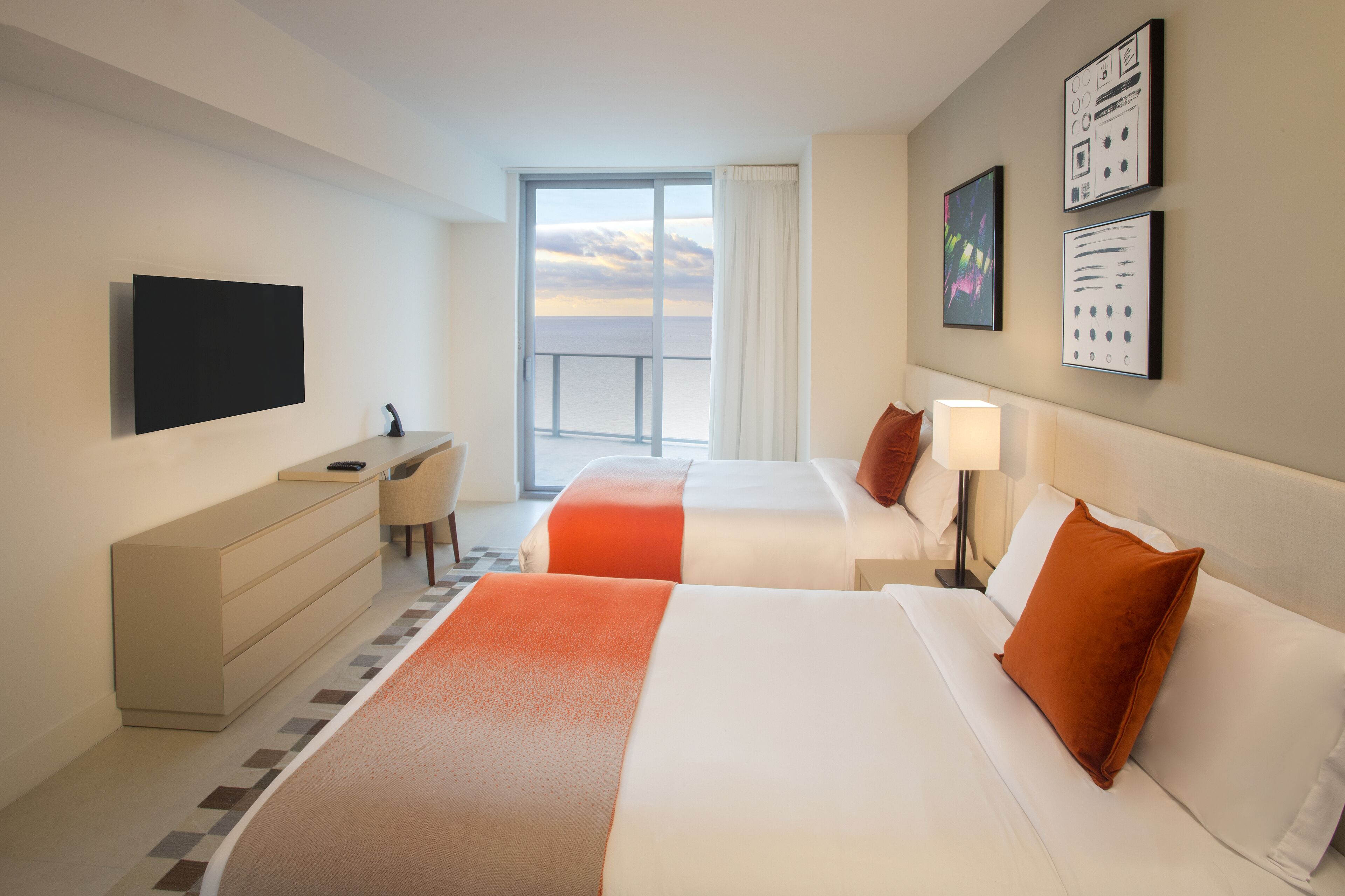 A hotel room with two beds, a desk, a TV, and a large window with a view.