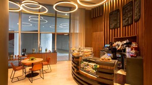 Un café moderno con interior de madera, una mesa redonda con sillas, una barra con una máquina de café y pizarras con el menú en la pared.