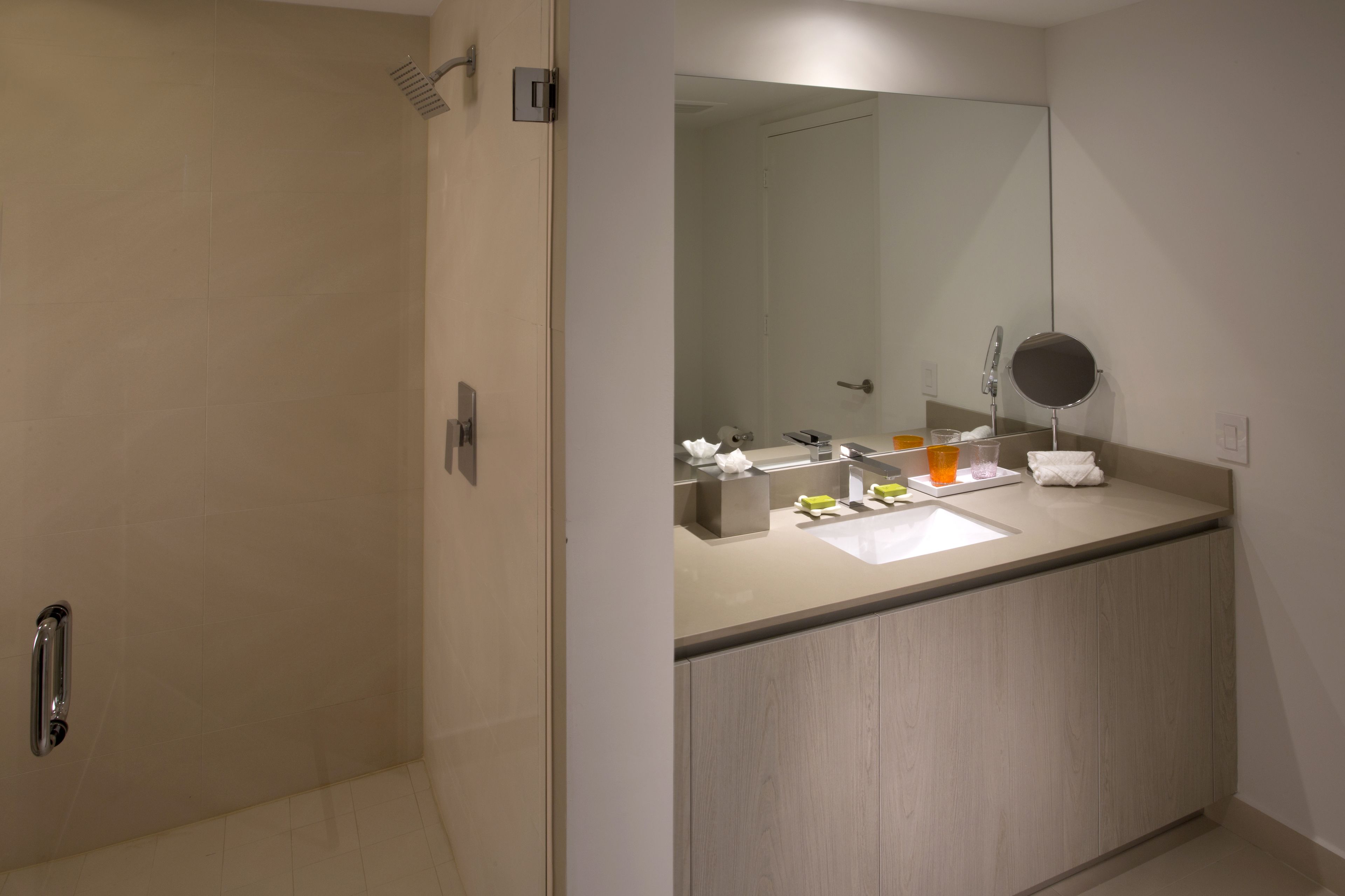 Une salle de bain moderne dotée d’une douche à l’italienne, d’un grand miroir et d’un meuble-lavabo avec des articles de toilette.