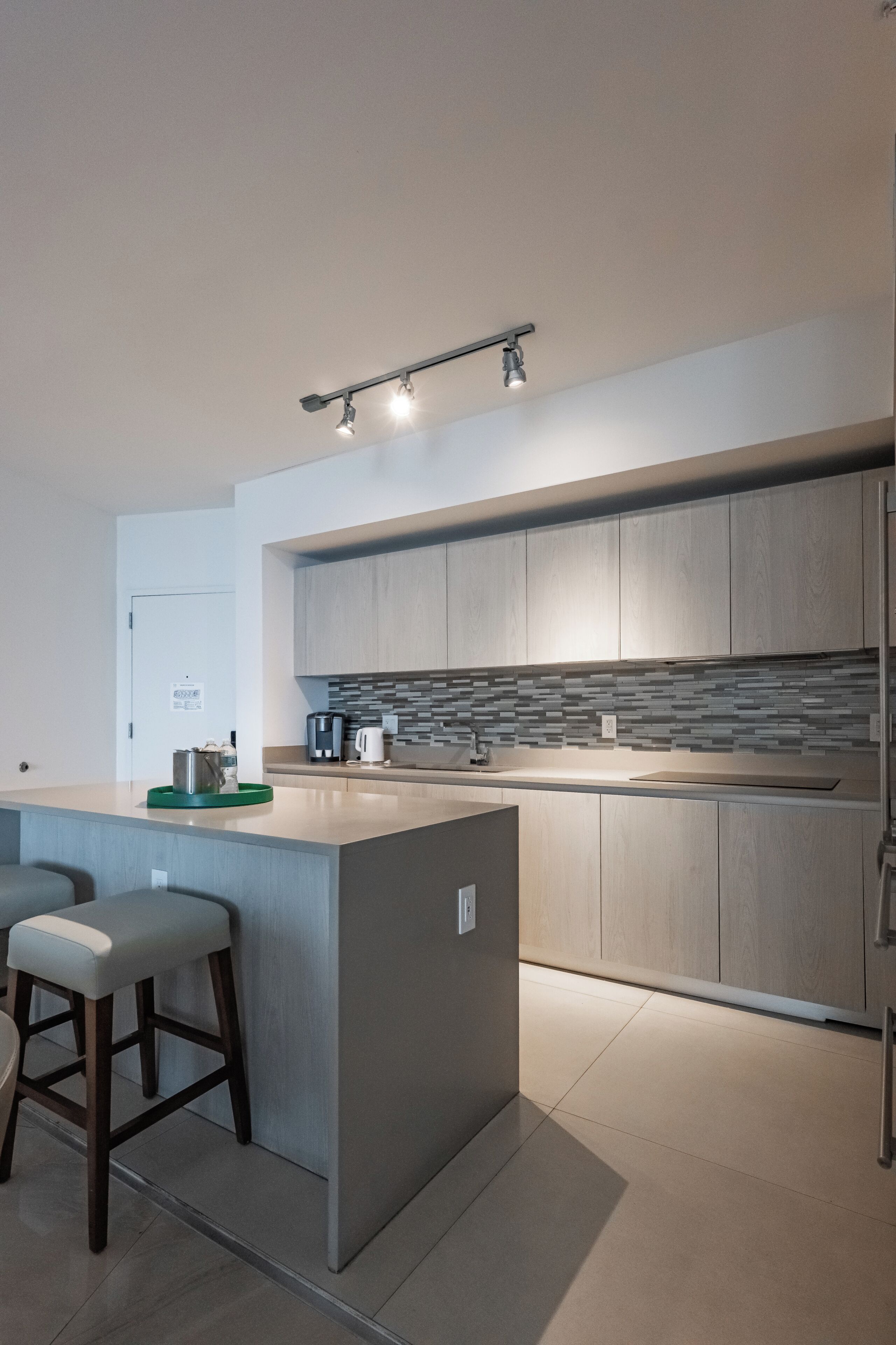 Een moderne keuken met een centraal eiland, barstoelen, een spatwand met een geometrisch patroon, en een plafondlamp.