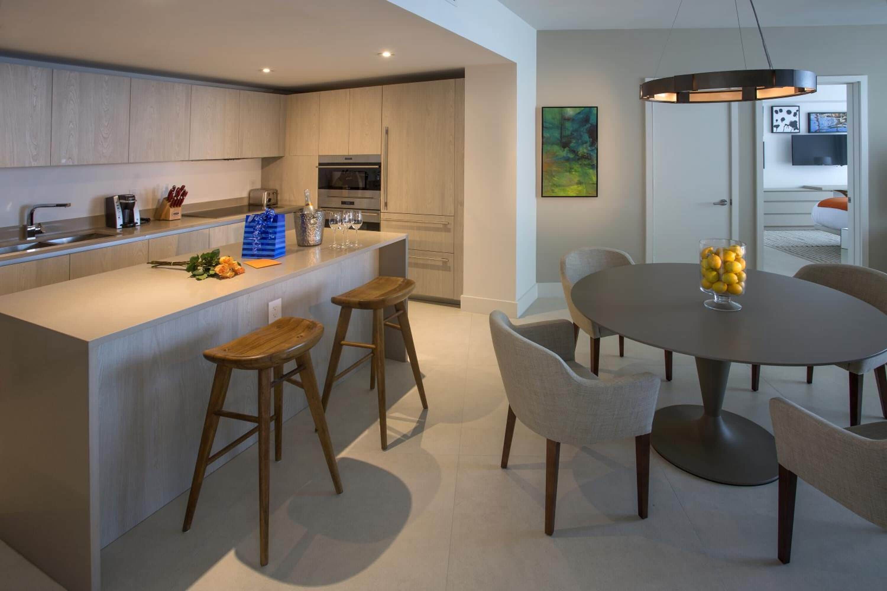 A modern kitchen with a central island, bar stools, and a dining table with chairs.