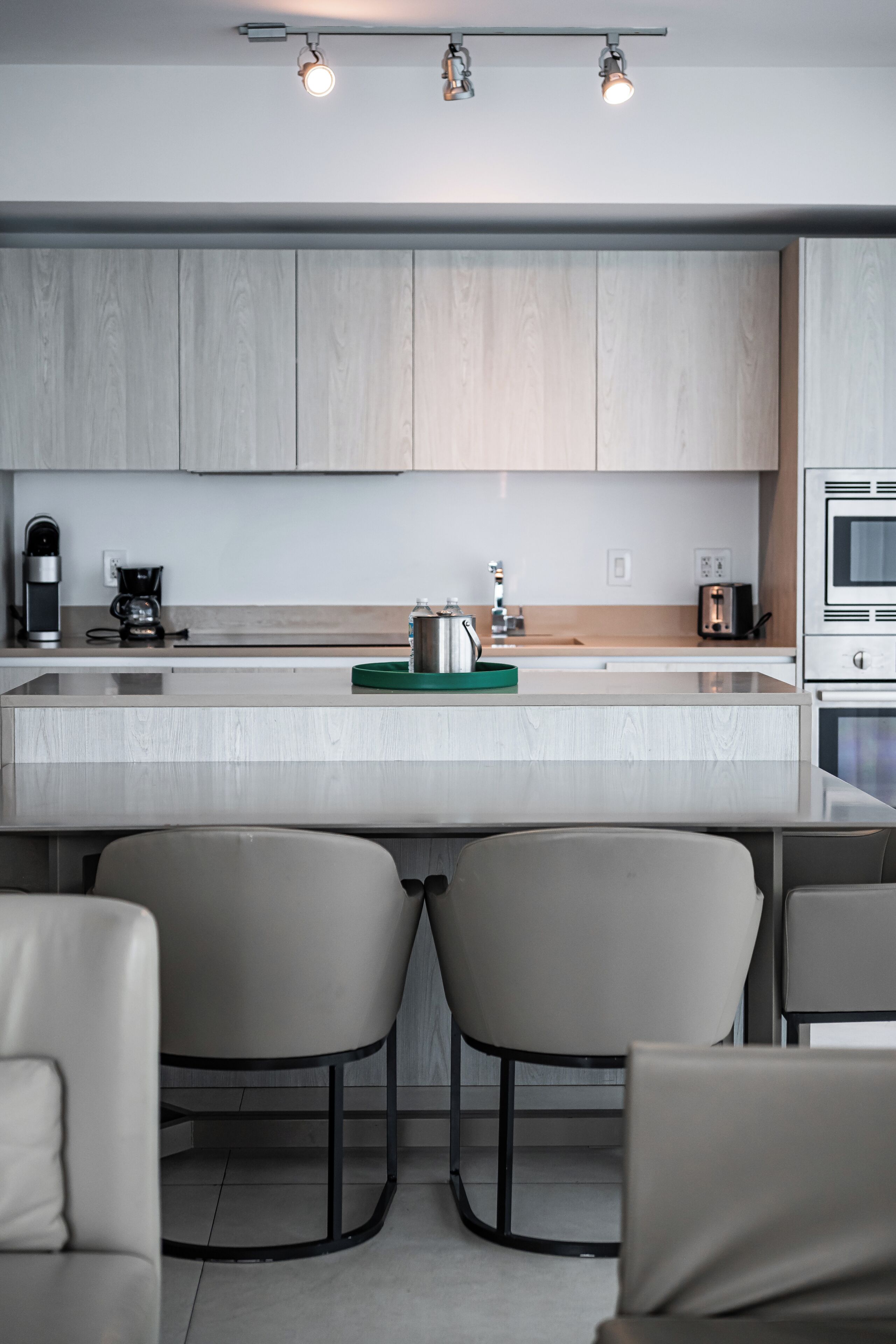 A modern kitchen with a central island, two bar stools, and a coffee maker.