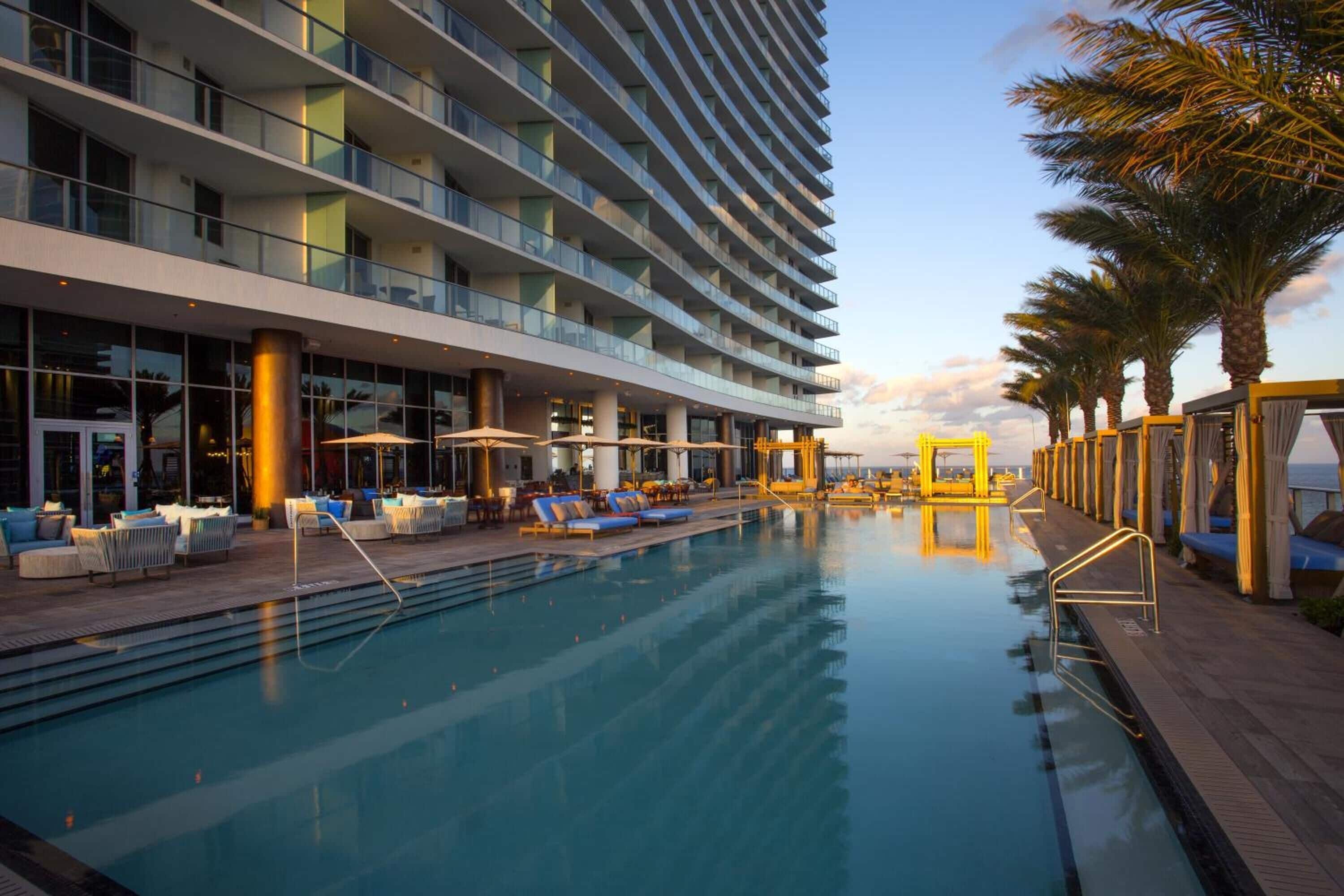 A modern hotel with a pool, outdoor seating, and palm trees.