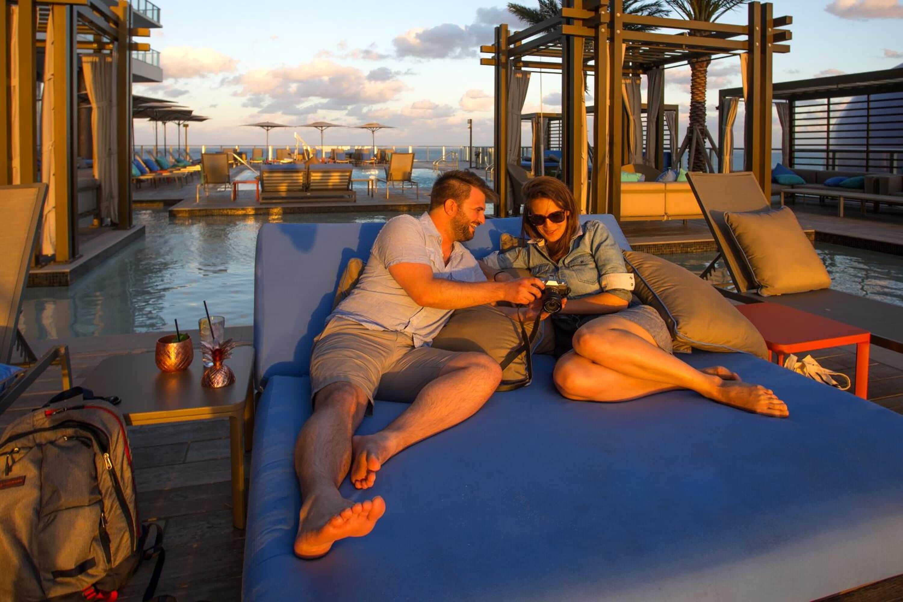 Um casal relaxando em espreguiçadeira à beira da piscina, com vista para o oceano.
