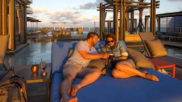 Um casal relaxando em espreguiçadeira à beira da piscina, com vista para o oceano.