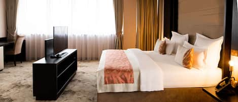 A hotel room with a large bed, a TV, a desk, and a window with curtains.