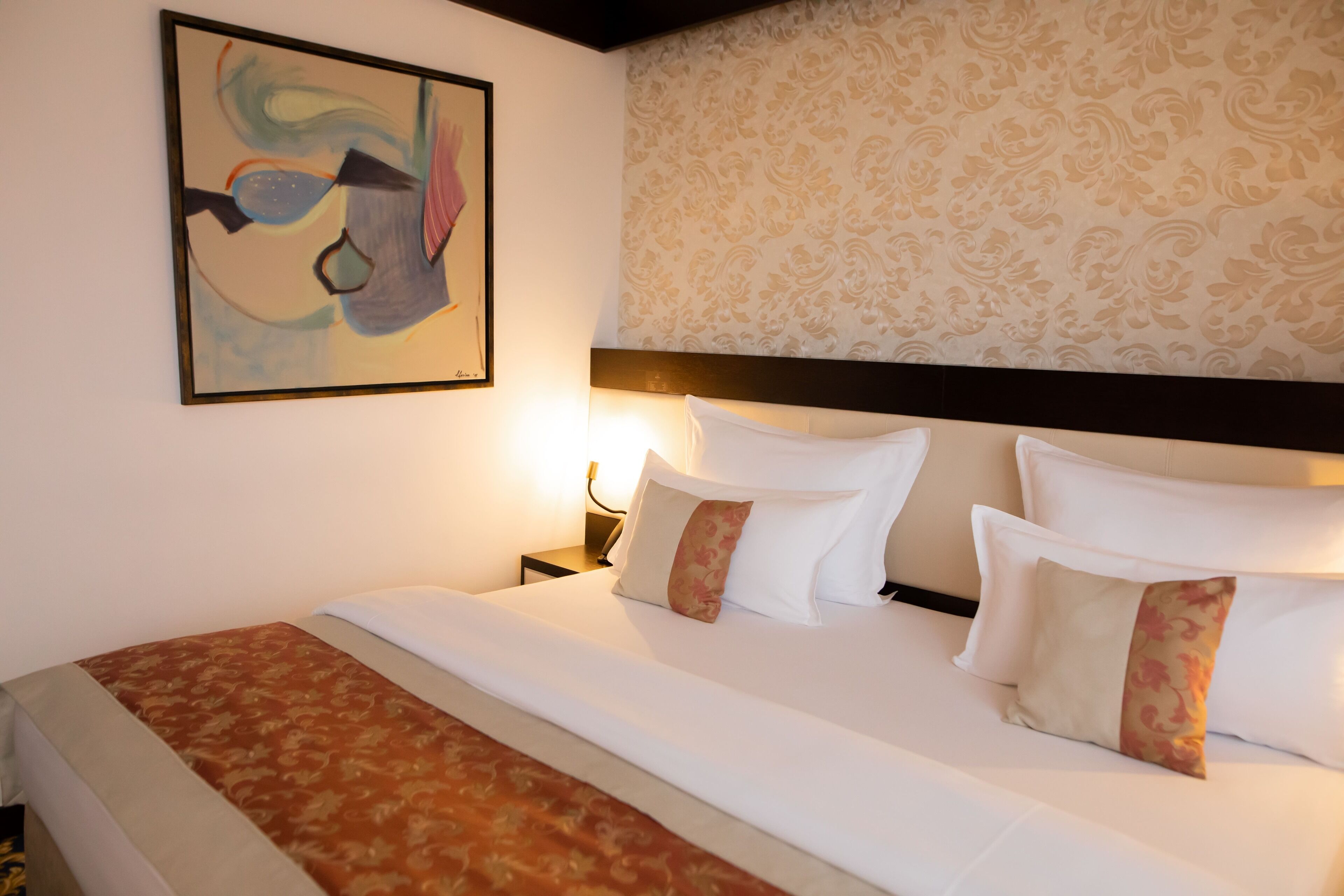 Habitació d'hotel amb un llit gran, un capçal, una tauleta de nit i un quadre penjat a la paret.