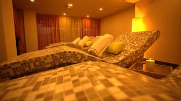 Een hotelkamer met twee bedden, beddengoed met een geruit patroon, een nachtkastje met een kaars en een raam met gordijnen.