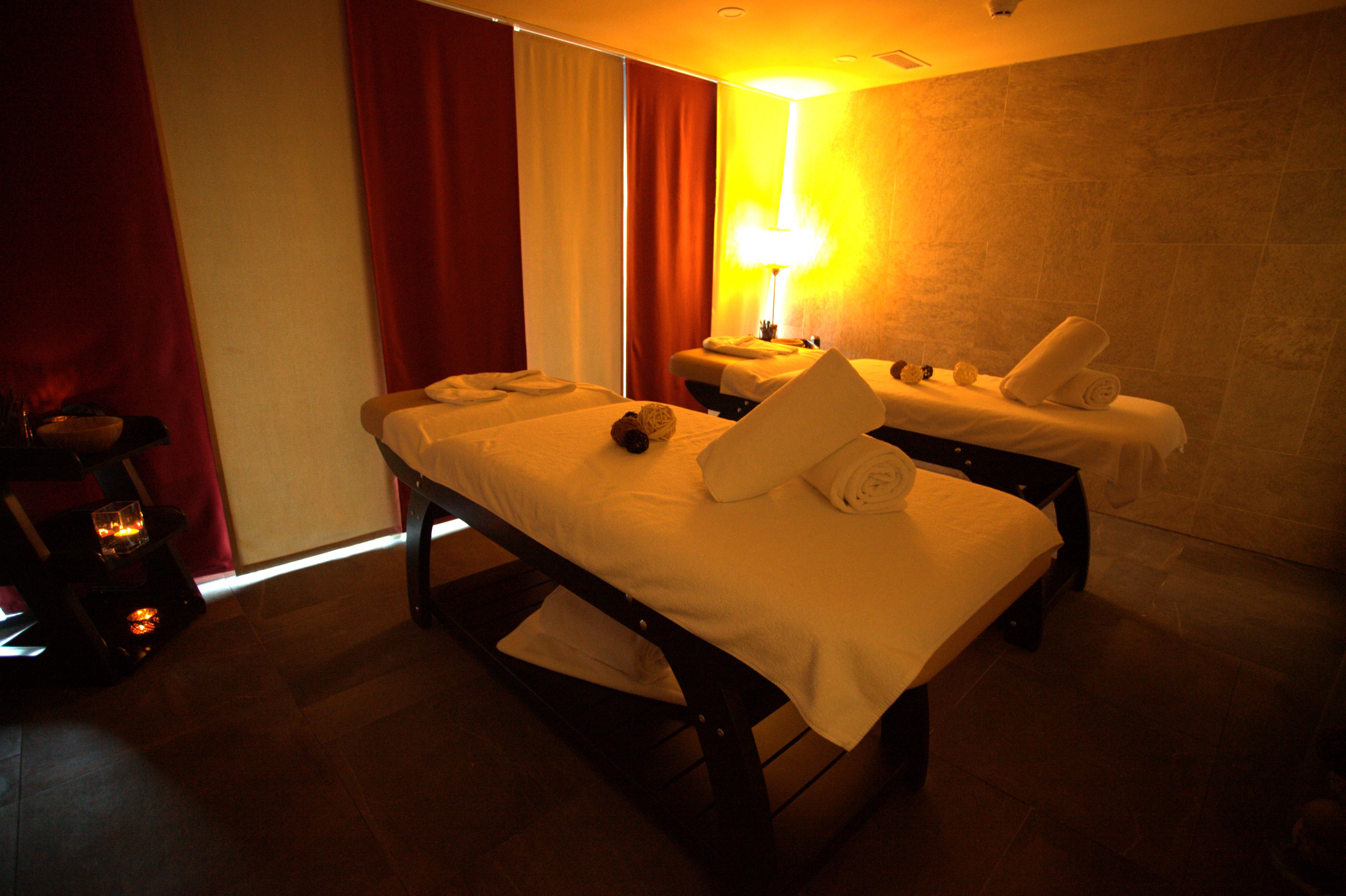A spa room with two massage tables, a massage chair, and a wall-mounted massage table.