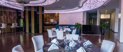 A modern hotel lobby with a round dining table set for four, surrounded by white chairs.