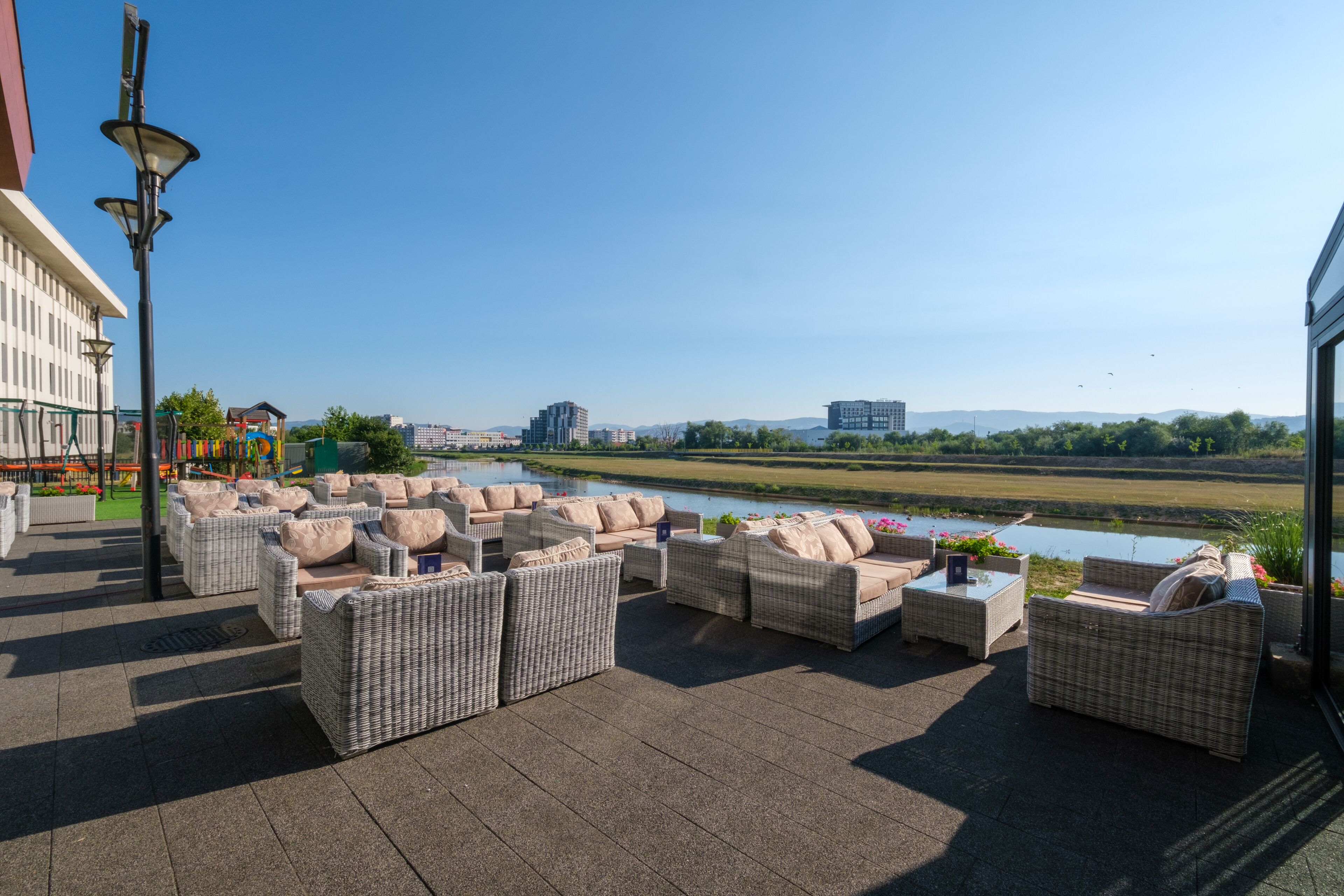 An outdoor seating area with wicker furniture and a view of a river and buildings in the distance.
