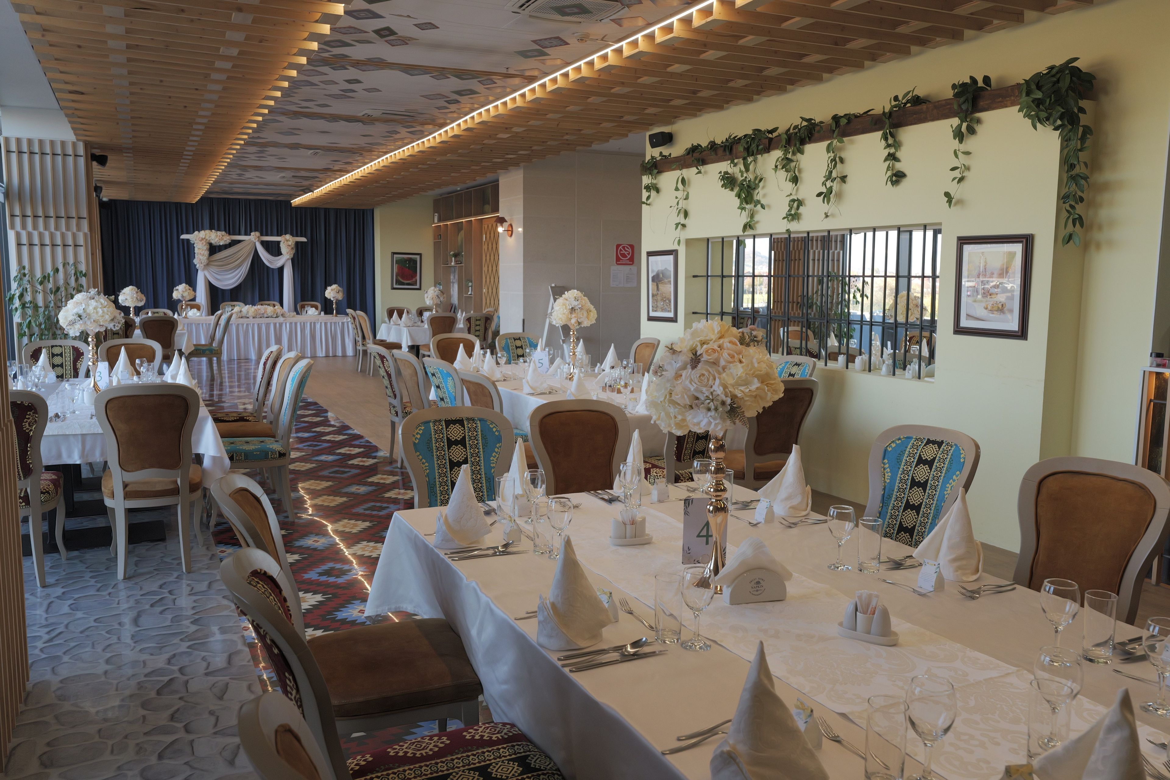A banquet hall with round tables, chairs, and floral centerpieces.