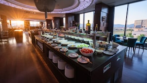 A buffet area with a variety of food items, a large window offering a view of the city, and a modern ceiling design.