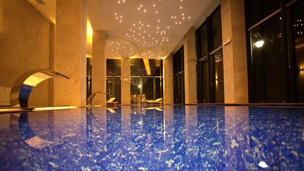 A spacious indoor swimming pool with a blue marble floor, large windows, and modern lighting fixtures.