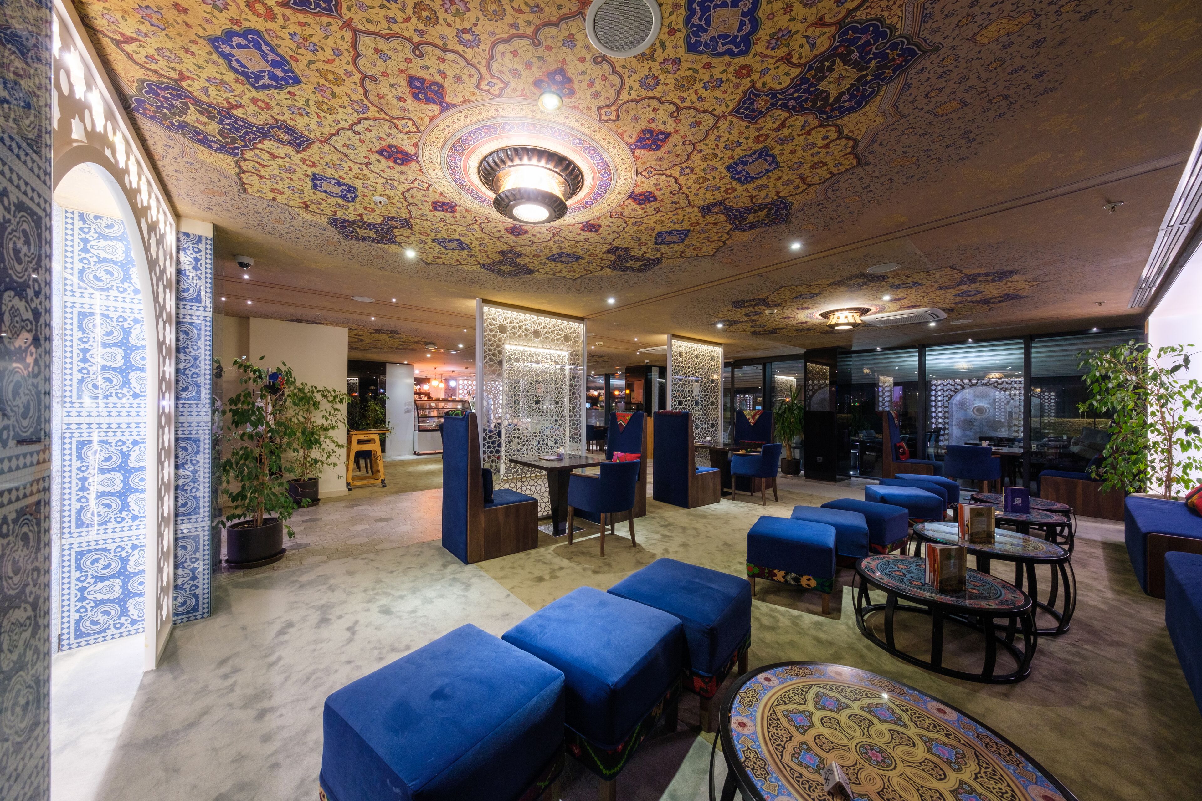 A hotel lobby with patterned ceiling, blue seating, and a central decorative light fixture.