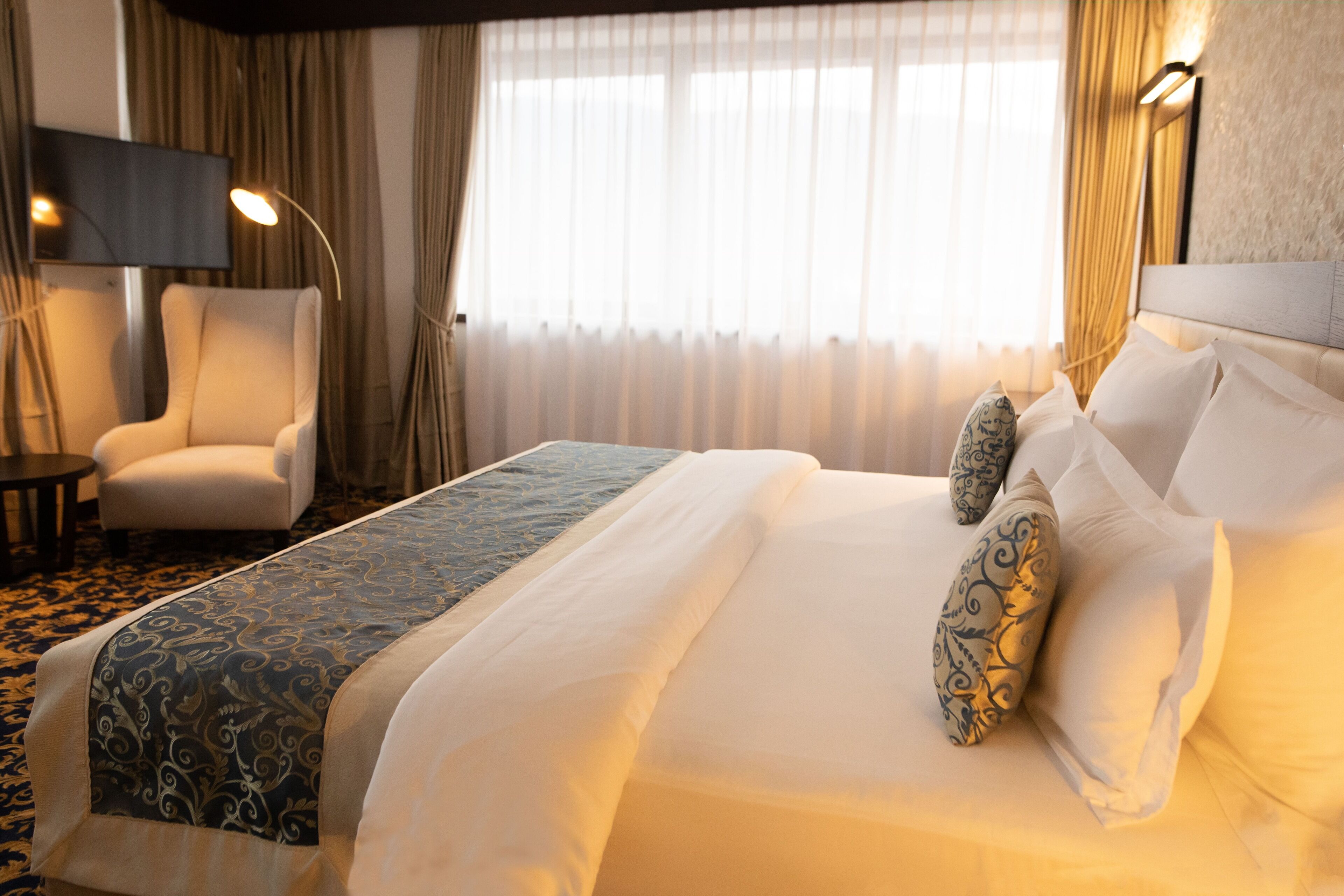 Une chambre d’hôtel avec un grand lit, une chaise, une télévision et des rideaux.