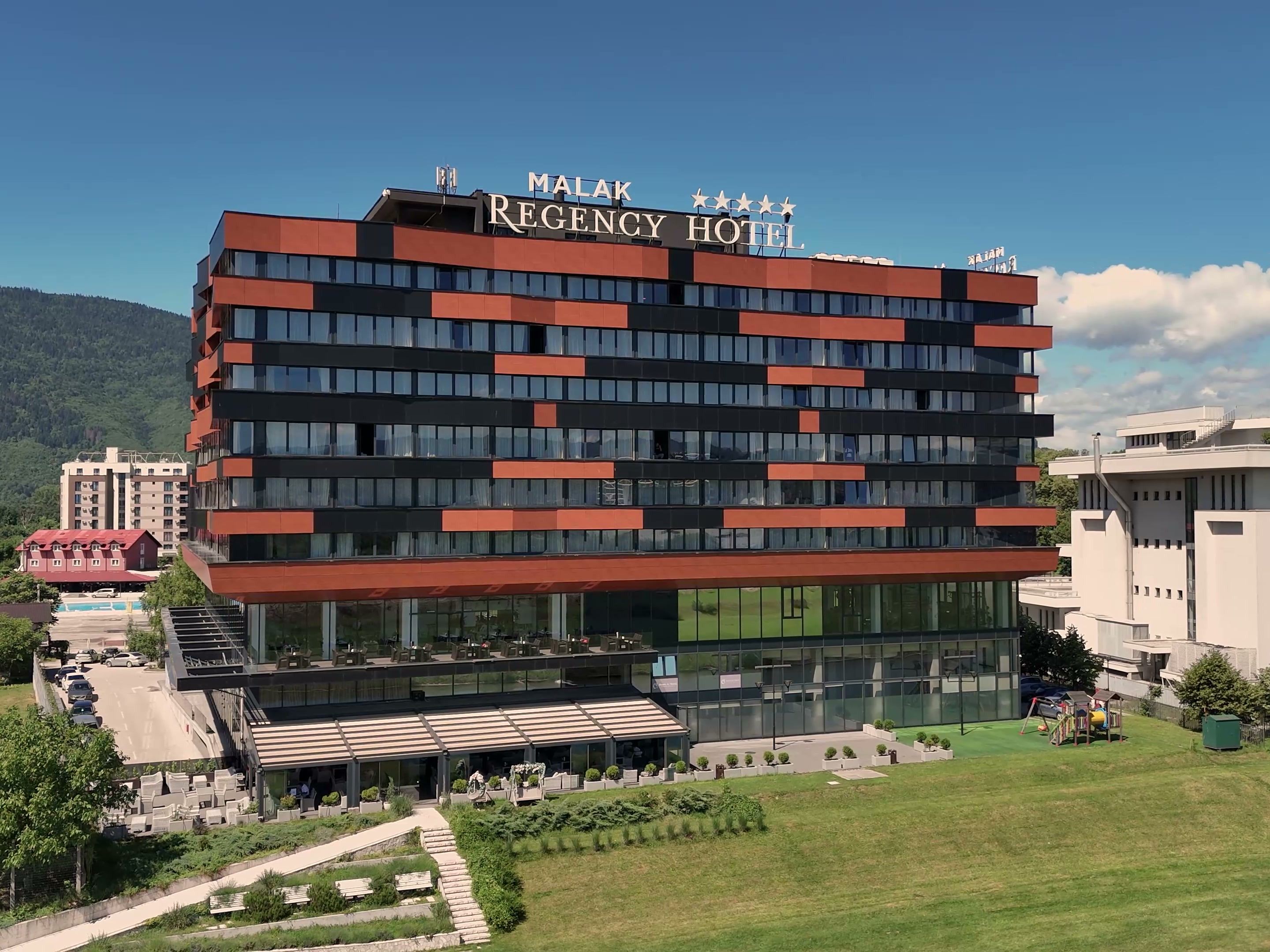 Un hotel de varios pisos con fachada moderna, un área de estar al aire libre y una vista despejada del paisaje circundante.