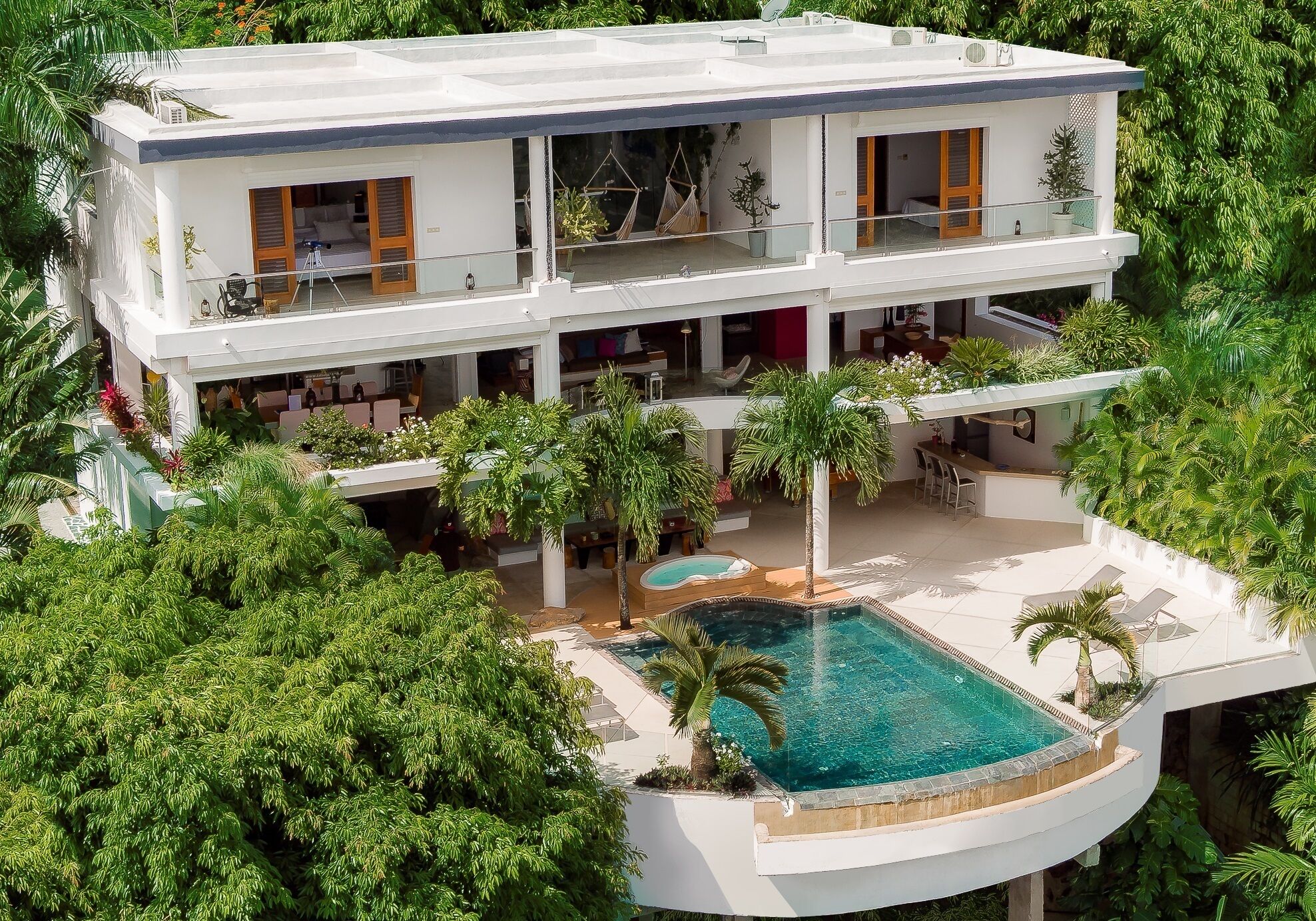 Una casa moderna de dos pisos con piscina, rodeada de exuberante vegetación.