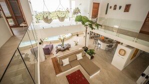 A spacious living area with a large sofa, a dining table, and a hanging chair. There is a staircase leading to an upper level with a balcony. - Casa Phil (Las Terrenas)