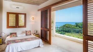 A bedroom with a bed, two windows with shutters, a ceiling fan, an air conditioning unit, and a balcony with a view of the ocean. - Casa Phil (Las Terrenas)