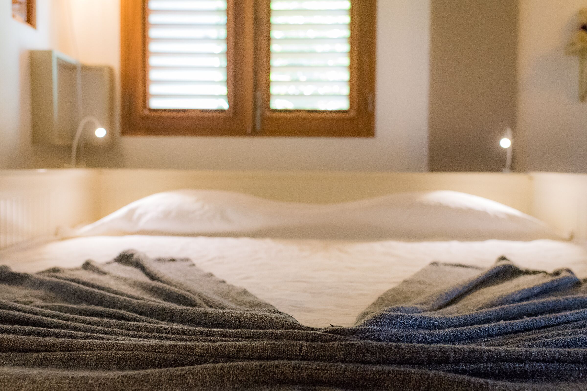 A bed with a striped blanket, a bedside lamp, and a window with blinds.