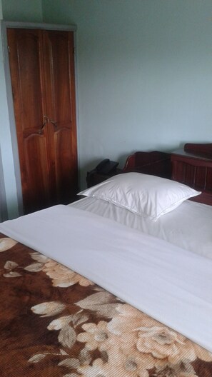 A bedroom with a bed, a wooden wardrobe, and a small desk with a telephone. - Kangle Plaza Hotel (Bamenda)