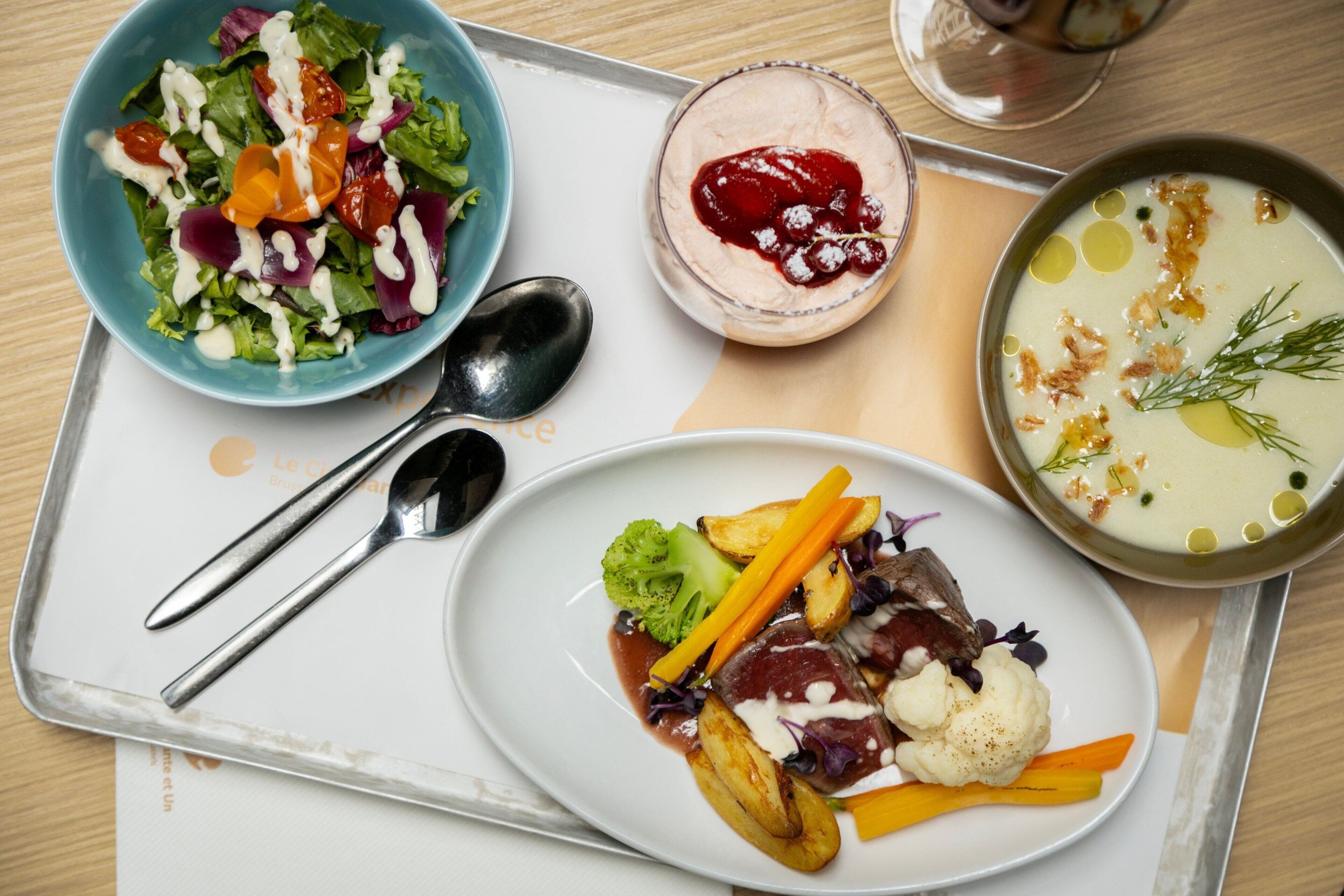 Una bandeja con una ensalada, un tazón de sopa y un plato de carne y verduras.