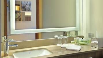Une salle de bain d’hôtel avec un grand miroir, un lavabo et divers produits de toilette disposés sur le comptoir.