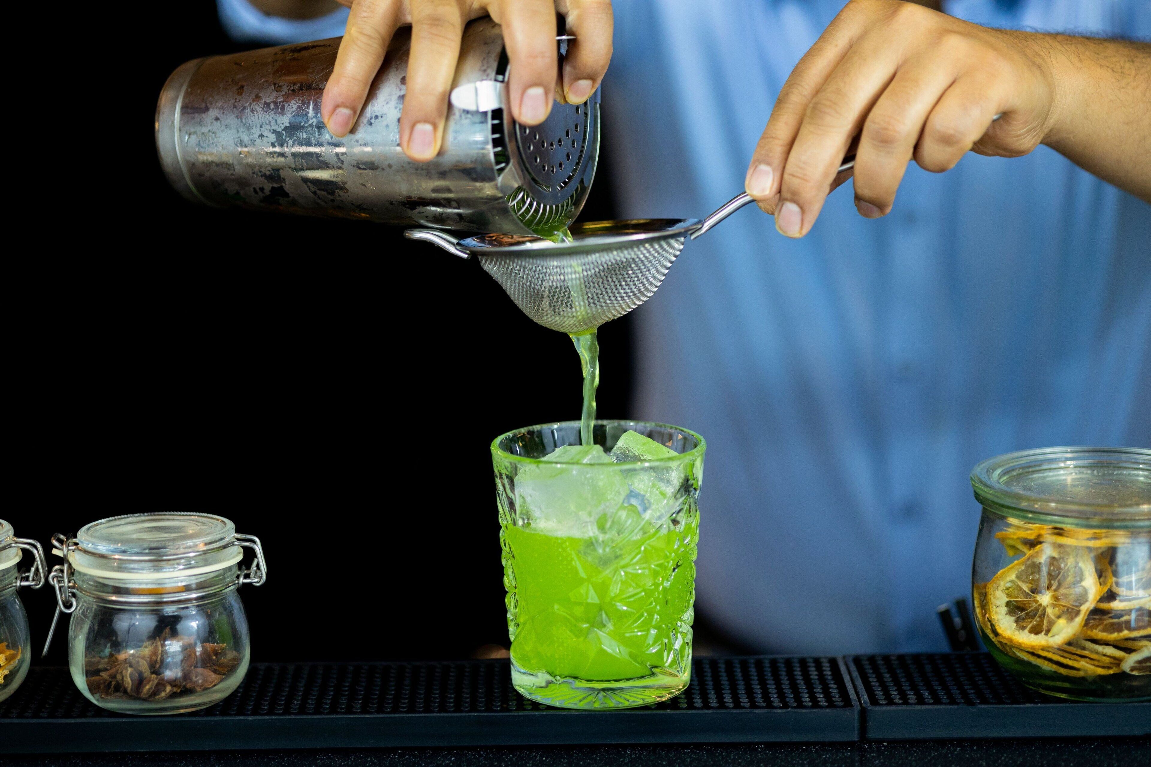 Un barman verse un liquide vert dans un verre.