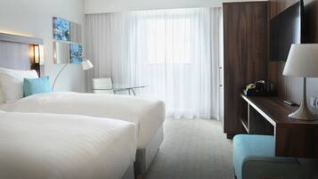 Habitación de hotel con dos camas grandes, un escritorio con televisor, una silla y una mesita.