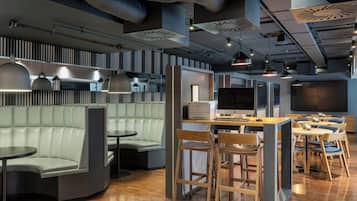 A modern restaurant with a bar area, seating arrangements, and a large screen.