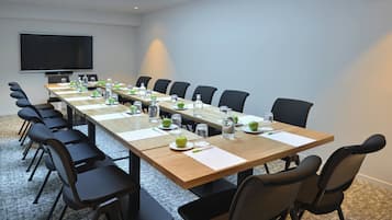 Une salle de conférence avec une longue table, des chaises, un téléviseur à écran plat et un sol recouvert de moquette.
