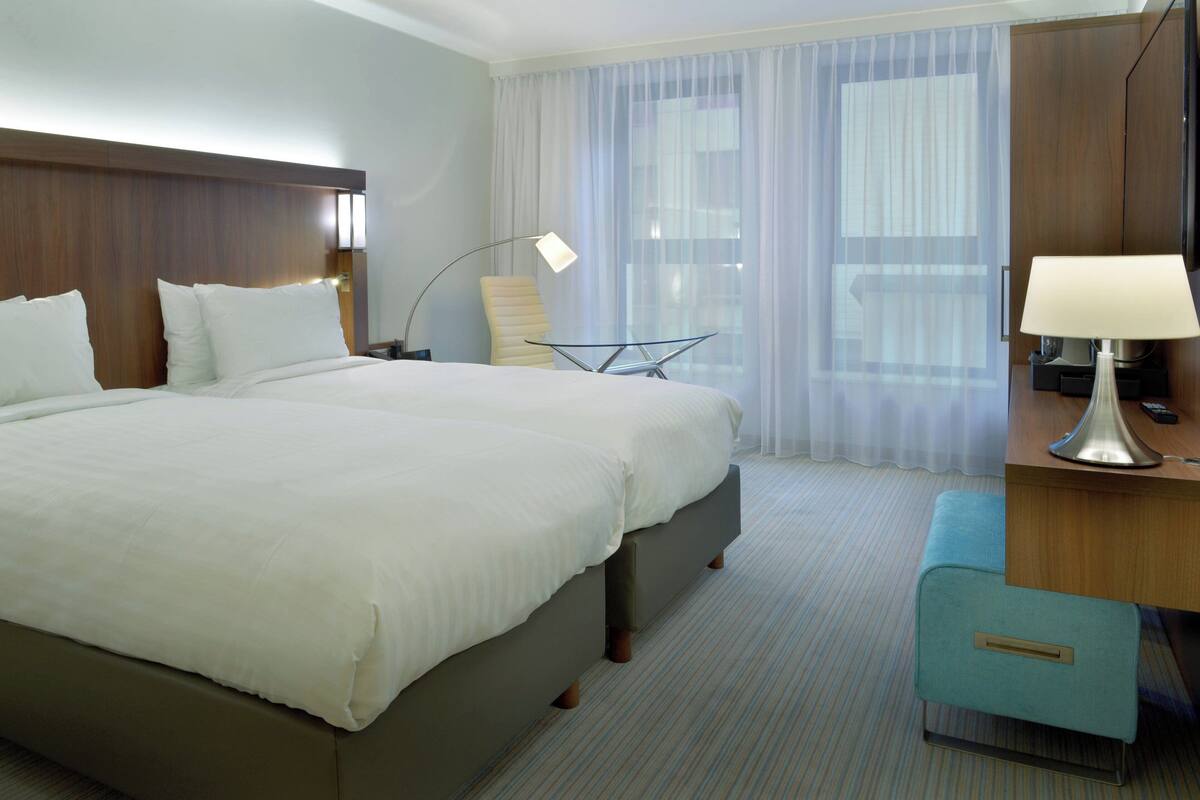 A hotel room with a large bed, a desk with a lamp, a chair, and a small table.