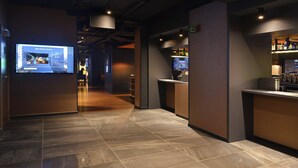 Un pasillo moderno de hotel con una pantalla digital, un mostrador de recepción y una zona de bar.
