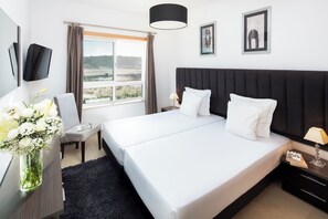 Relax in a spacious room with a large bed, desk, and flat-screen TV, offering a view of the outdoors through a window with curtains.