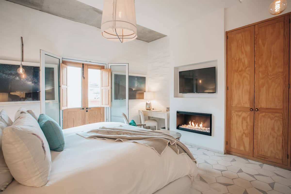 Un dormitorio moderno con una cama grande, una chimenea, un armario y un escritorio con una silla.