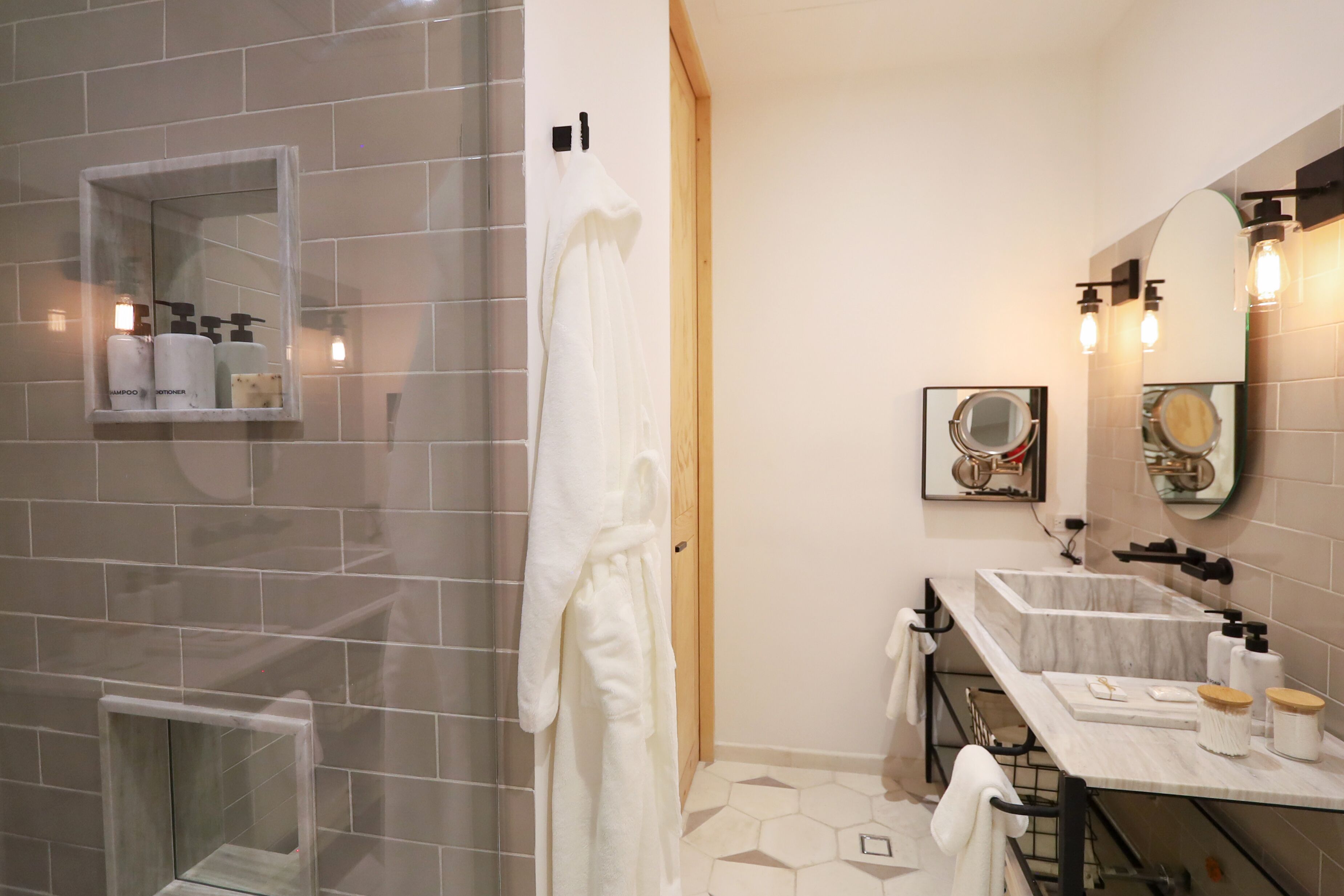 Un baño moderno con cabina de ducha de vidrio, tocador con lavamanos de mármol e iluminación empotrada en la pared sobre el espejo.