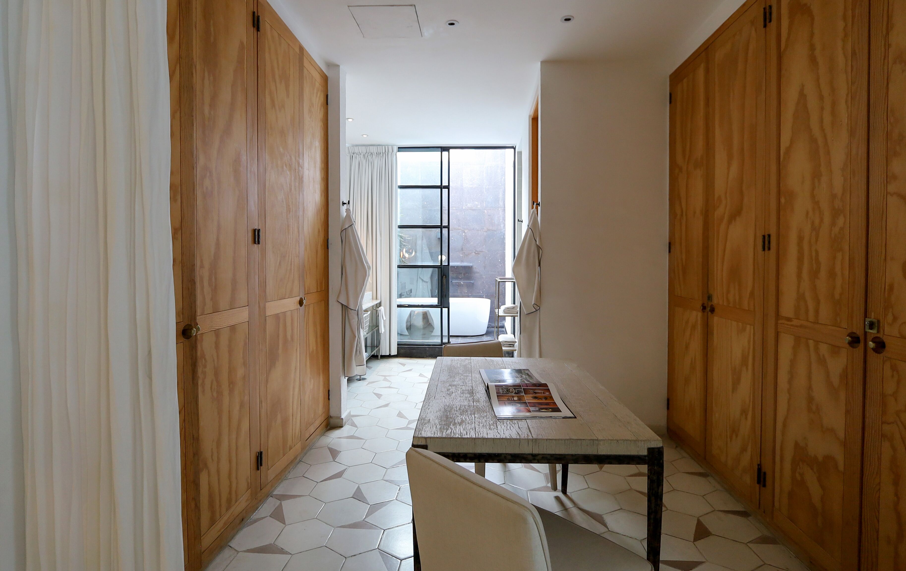 Un pasillo con armarios de madera, piso de baldosas y una mesa con una revista.