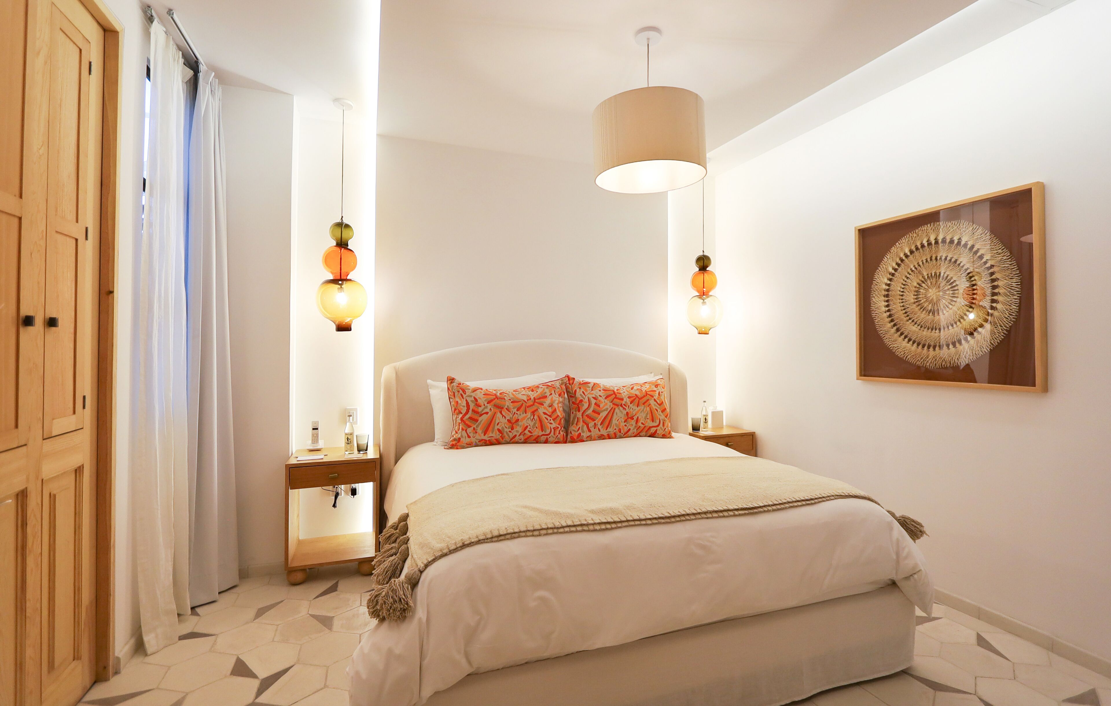 A bedroom with a bed, bedside tables, a hanging light fixture, a wooden wardrobe, and a wall-mounted artwork.