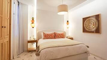 A bedroom with a bed, bedside tables, a hanging light fixture, a wooden wardrobe, and a wall-mounted artwork.