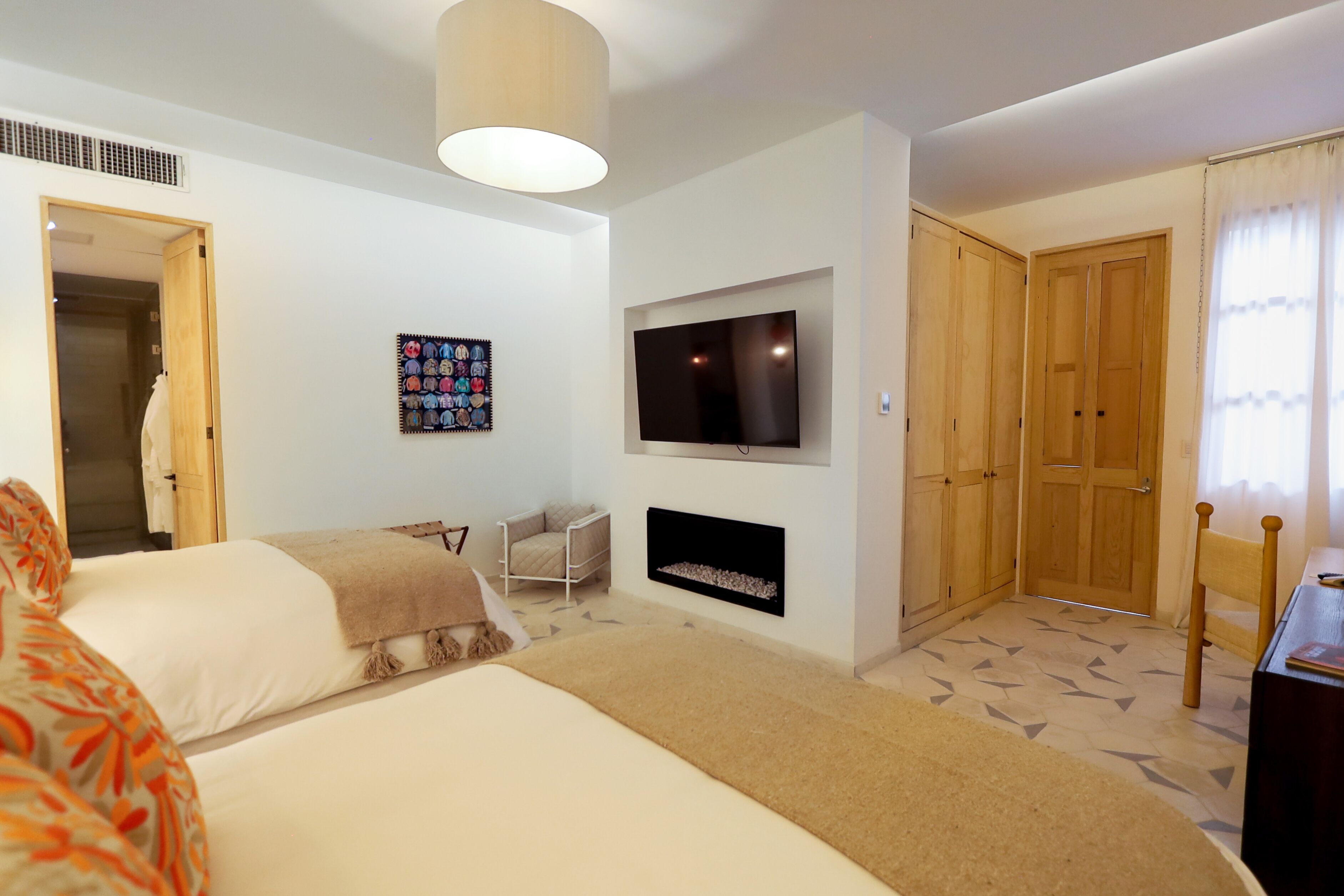 Habitación de hotel con cama, televisor montado en la pared, chimenea, armario y puerta que da a otra habitación.